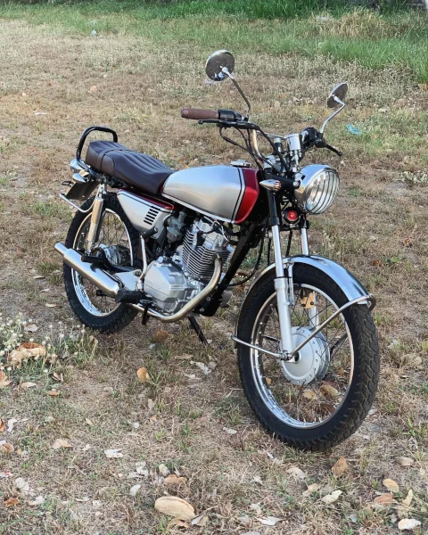Classic silver and maroon motorcycle with chrome details parked on dry grass, capturing a vintage, nostalgic vibe against a blurred green background.